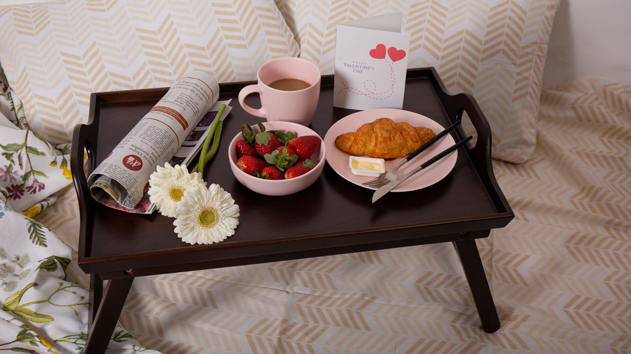 A beautiful breakfast, flowers and a newspaper arranged on a wooden tray